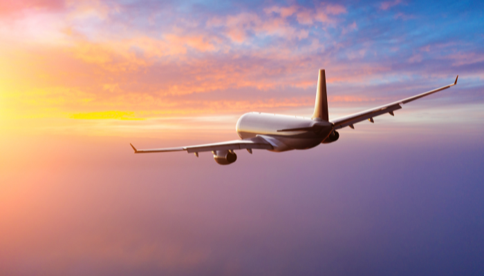A commercial airplane descends towards a landing at an airport near London, with the city skyline and skyscrapers in the background, symbolizing the international travel and mobility impacted by the UK’s digital eVisa transition.